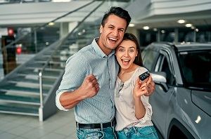 couple smiling at camera holding keys to new car
